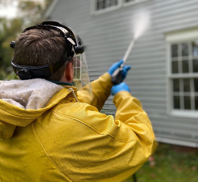 A man in yellow jacket spraying water on a house.